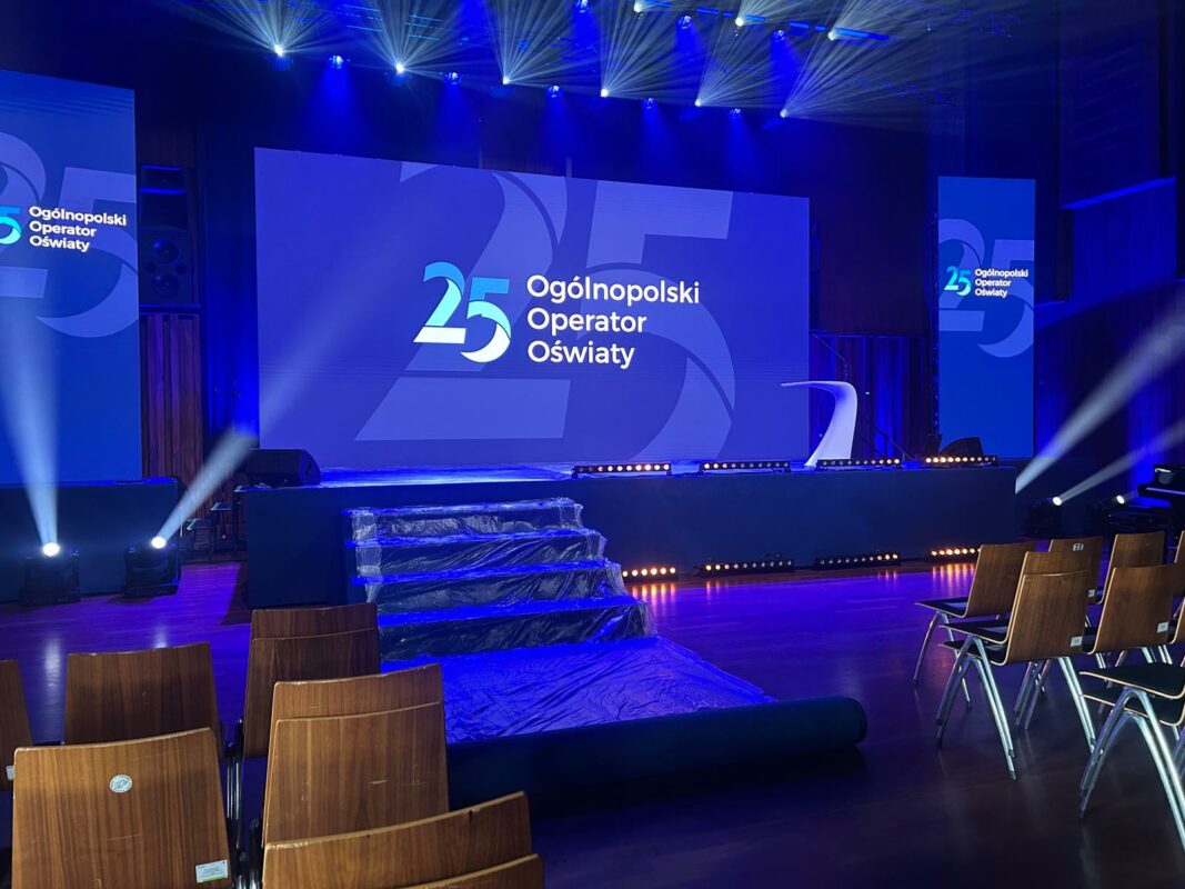 Scena przygotowana do uroczystej gali, z profesjonalnym oświetleniem, ekranem multimedialnym i scenografią, na której konferansjerka Katarzyna Głuchowska poprowadzi wydarzenie.